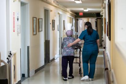 Care aide helping senior walk down hospital hallway